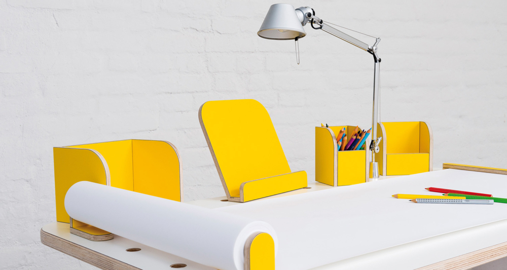 Ansicht auf den growing table mit weißer Oberfläche und gelben Tools mit einer angebrachten Tischlampe sowie ausgerollten Papierrolle mit Stifen