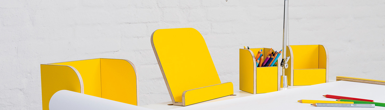 Ansicht auf den growing table mit weißer Oberfläche und gelben Tools mit einer angebrachten Tischlampe sowie ausgerollten Papierrolle mit Stifen