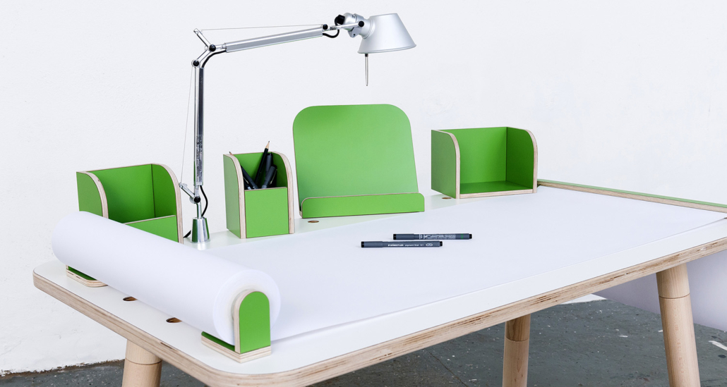 Ansicht auf den growing table mit weißer Oberfläche und grünen Tools mit einer angebrachten Tischlampe sowie ausgerollten Papierrolle mit Stifen
