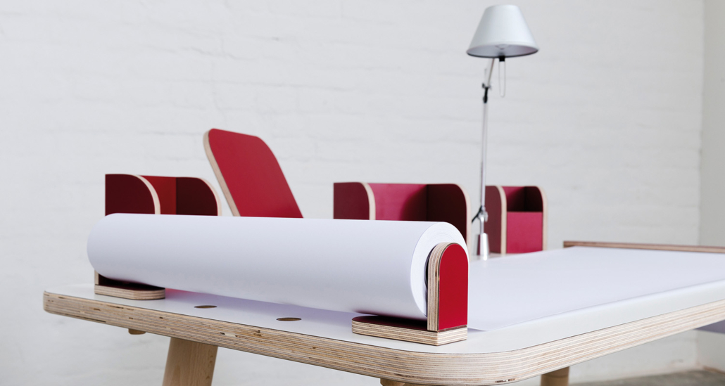 seitliche Ansicht auf den growing table mit weißer Oberfläche und roten Tools mit einer angebrachten Tischlampe sowie ausgerollten Papierrolle