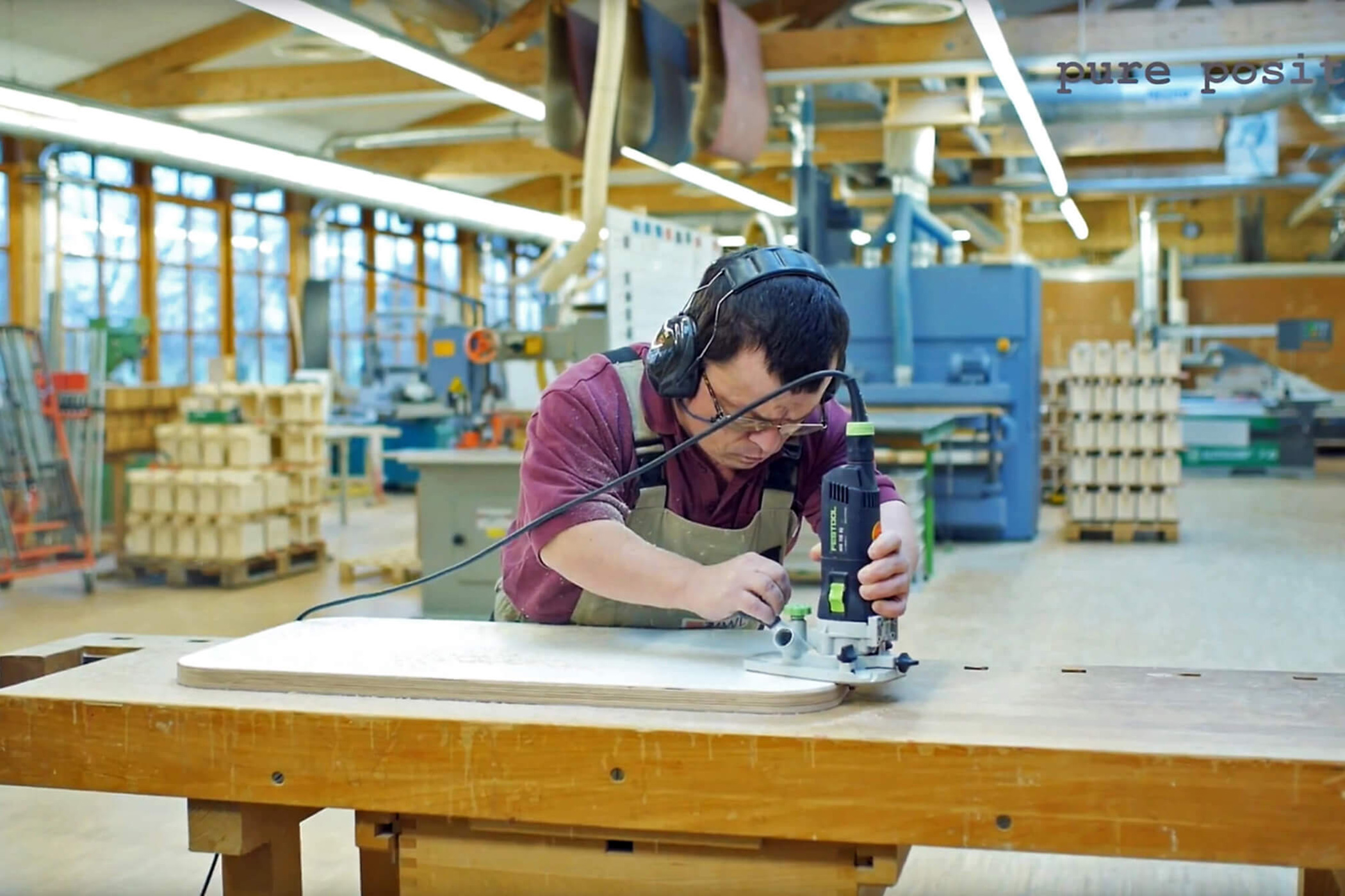 Mitarbeiter von der IWL schleift mit einem Schleifgerät die Oberfläche einer Tischplatte in der Produktion