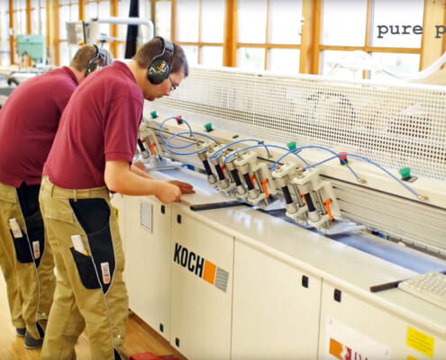 Mitarbeiter von der IWL arbeiten an einer länglichen Bandmaschine ein Holzstück in der Produktion