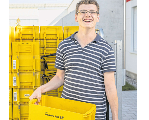 Titelbild vom Magazin FR7 mit einem glücklichen Menschen mit Behinderung der eine gelbe Wanne von der Deutschen Post hält und im Hintergrund mehrere Wannen stehen