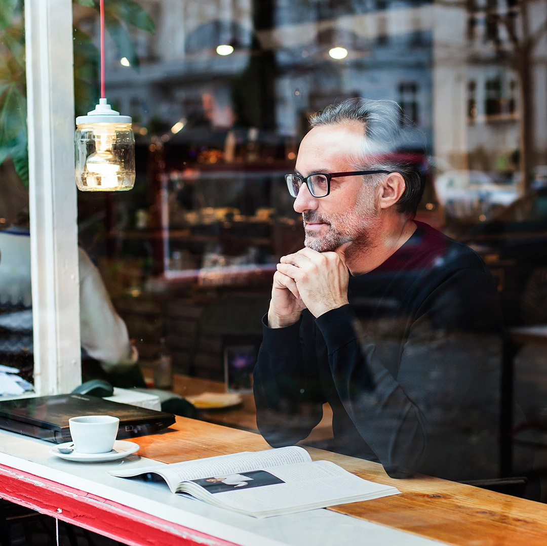 Olaf Schröder, Designer von pureposition, sitzt hinter einer Glaswand in einem Kaffee und schaut dabei raus